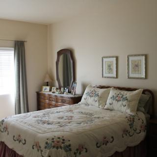 A cozy and neatly arranged bedroom featuring a large quilted bed, elegant mirror, and framed pictures on the wall.
