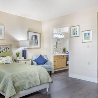 A cozy bedroom with a green bedspread, decorated with tasteful artwork and an adjacent view into the bathroom.