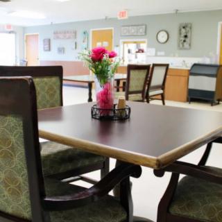 A brightly lit dining area with a table and chairs, featuring a floral centerpiece.