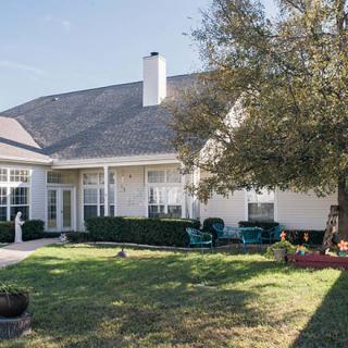 A cozy backyard with patio furniture and a large tree, showcasing a well-maintained lawn in front of a charming house.