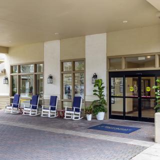 A welcoming building entrance with rocking chairs and potted plants along a covered walkway.