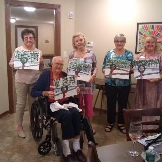 A group of seniors proudly displaying their artwork indoors.