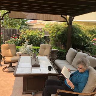A person reading on a comfortable patio surrounded by garden greenery.