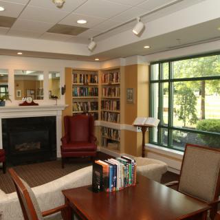 A cozy library reading area with bookshelves, comfortable seating, and a fireplace.