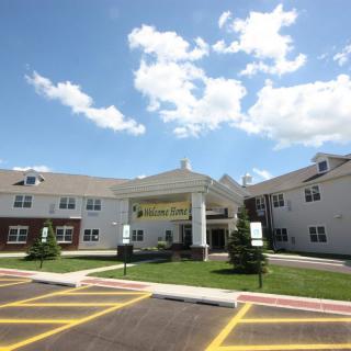 A two-story residential building with a main entrance and parking lot under a cloudy sky.