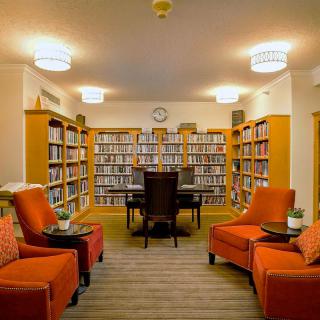 A cozy library room with bookshelves, comfortable chairs, and a central table.