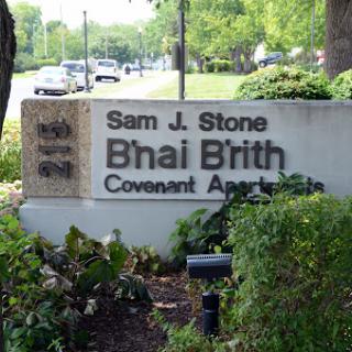 A sign for the Sam J. Stone B'nai B'rith Covenant Apartments, showcasing the building's identity in a landscaped area.