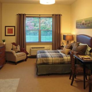 A cozy bedroom with warm lighting, featuring a bed, armchair, and desk.