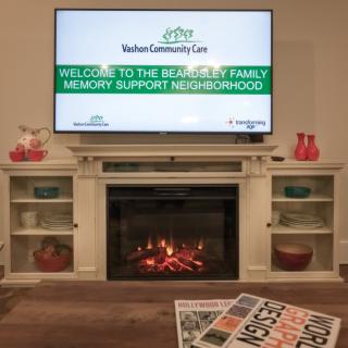 A cozy living room setup with a television above a fireplace, featuring homey decor.