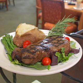 A delicious steak dinner served with a baked potato, asparagus, cherry tomatoes, and fresh greens.