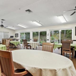 A spacious dining room with several tables and chairs, featuring large windows and green tablecloths.