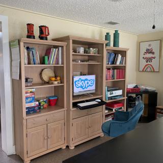 A living room features a wooden bookshelf with books, decorative items, and a computer setup.