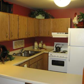 A cozy kitchen with wooden cabinets, red walls, and essential appliances.