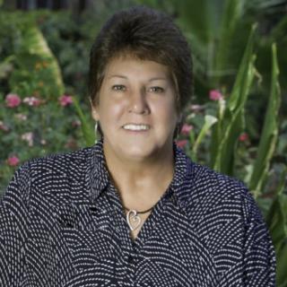 A person sitting outdoors with a garden backdrop.