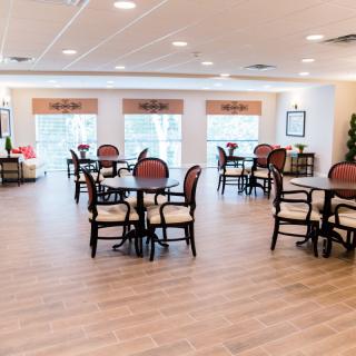 A spacious and elegantly designed dining area with multiple tables and chairs, featuring wooden flooring and large windows.