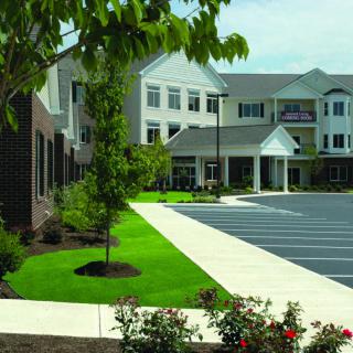A modern building with a landscaped front and a parking lot.