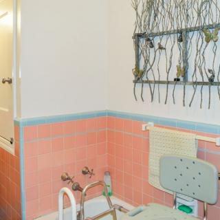 A bathroom with safety features including handrails and a chair in the tub, alongside decorative wall art.