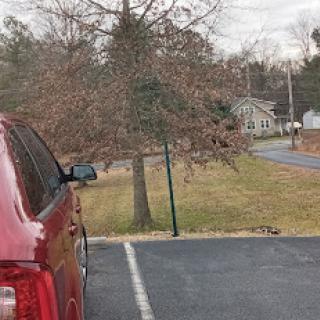 A red vehicle parked beside a grassy area, with trees in the background and a road leading away.
