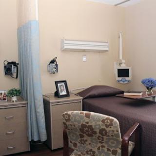 A well-equipped hospital room featuring a bed, bedside furniture, and personal touches.