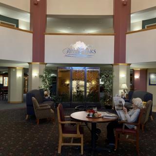 A cozy lobby area with comfortable seating and decorative plants, where elderly individuals enjoy a conversation.