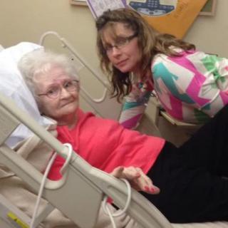 A young woman visits an elderly woman in a hospital bed.