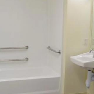 A clean, white bathroom featuring a bathtub with grab bars and a simple sink.