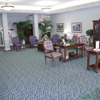 A well-decorated waiting room with chairs and tables, featuring plants and paintings.