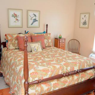 A cozy bedroom featuring a wooden four-post bed with floral bedding and coordinating pillows, complemented by framed botanical artwork on the walls.