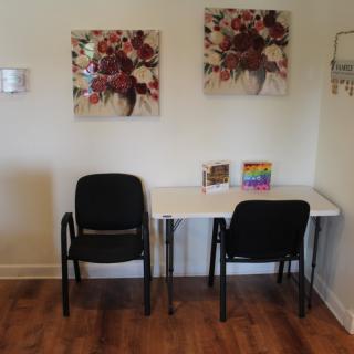 A small waiting area with two chairs and a table, decorated with artwork on the wall.