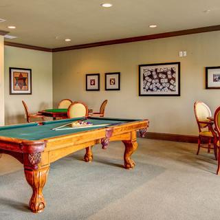 A recreational room featuring a pool table, surrounded by chairs and decorated with framed photographs on the walls.