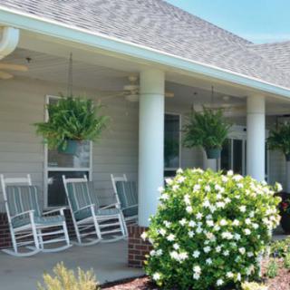 A cozy porch with rocking chairs, hanging plants, and lush greenery.