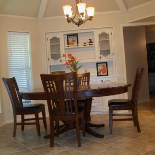 A cozy dining room featuring a wooden table with matching chairs, illuminated by a chandelier, with decorative shelving in the background.