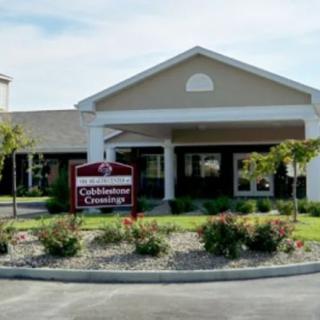 A building entrance with a sign and landscaped area in front of a parking lot.