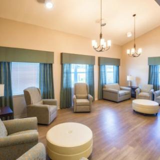 A cozy living room with armchairs and chandeliers, featuring wooden floors and elegant curtains.