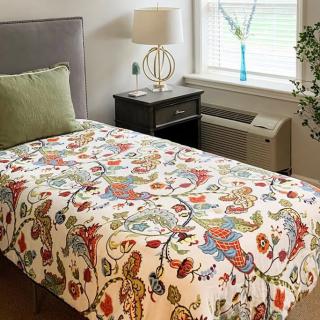 A cozy bedroom with a colorful quilt, a pillow on the bed, and a nightstand by the window.