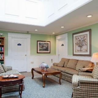 A cozy living room with green walls, featuring a sofa set, coffee tables, and artwork under a skylight.