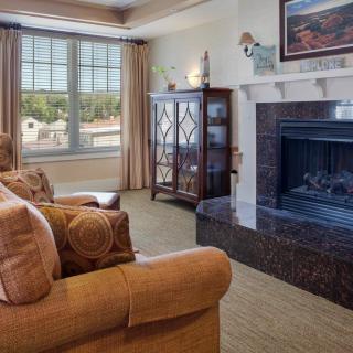 A cozy living room featuring a comfortable sofa and armchair set near a fireplace, with a large window providing natural light.