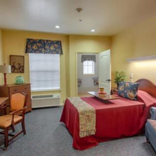 A cozy bedroom with warm yellow walls, featuring a bed with red bedding and a small desk and chair by the window.