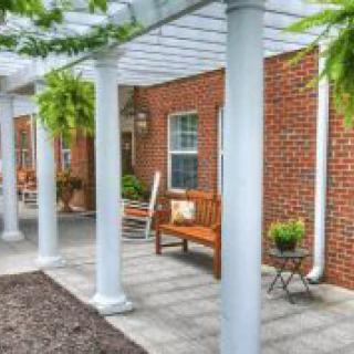 A cozy patio with a pergola, featuring benches and plants alongside a brick wall.