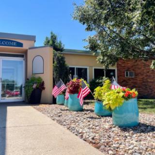 A well-maintained building entrance with colorful plants and small American flags displays a welcoming atmosphere on a sunny day.