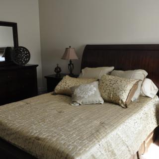 A cozy bedroom with a neatly made bed and decorative pillows, featuring a wooden headboard and matching furniture.