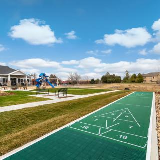 A scenic park featuring a shuffleboard court and playground under a clear blue sky.