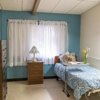 A tidy hospital room with a single bed, dresser, and flowers by the window.