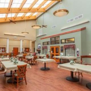 A spacious dining hall with tables and chairs, featuring large skylights and wooden flooring.