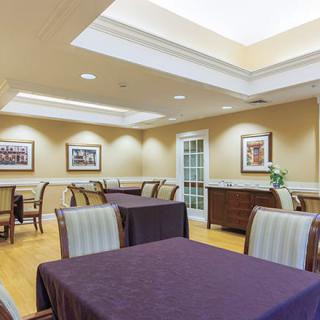 A well-lit dining room with neatly arranged tables and chairs, adorned with framed artwork on the walls.
