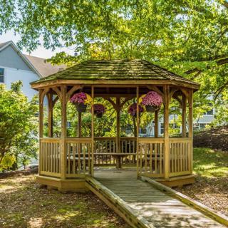 A charming wooden gazebo surrounded by greenery and hanging flowers.