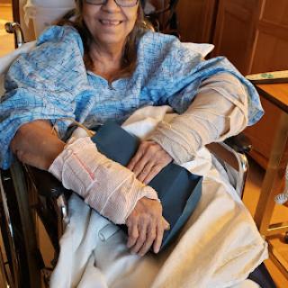 A patient in a wheelchair, wrapped in a hospital gown, resting with bandaged arms.