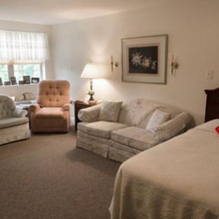 A cozy living space featuring a sofa, armchair, and a bed with soft lighting from a lamp by the window.