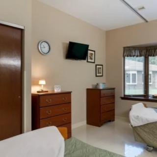 A minimalist bedroom with furniture, including dressers, a wall-mounted television, and a window allowing natural light.