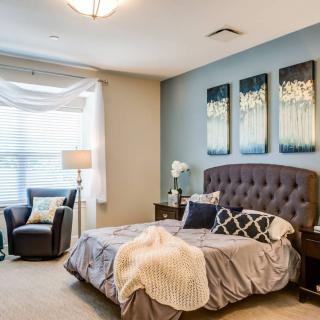 A beautifully decorated bedroom with modern furniture and artwork, featuring a comfortable bed and ample natural light.